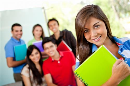 Female student with green notebeook in foreground with group of 5 students in background 